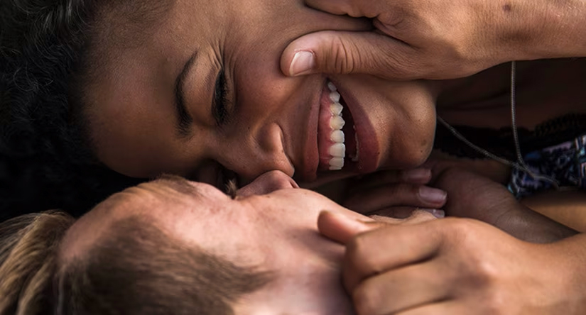 Gros plan sur un couple complice. Une femme noire rit aux éclats tandis que son partenaire lui caresse le visage.