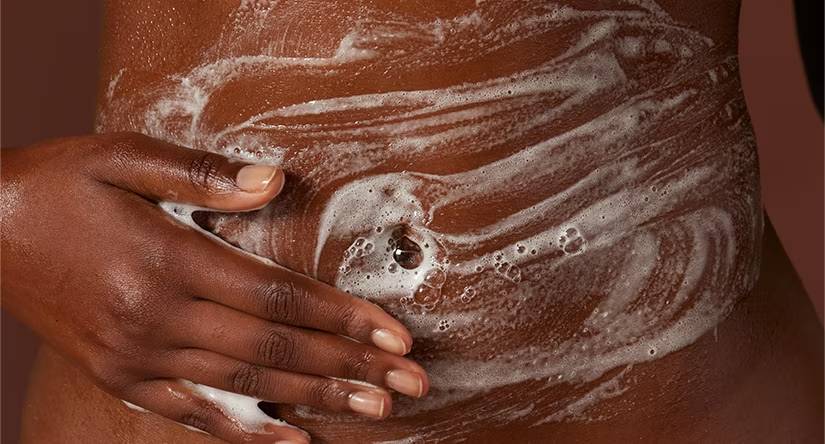 Gros plan sur une femme noire qui savonne délicatement son ventre avec une mousse riche.