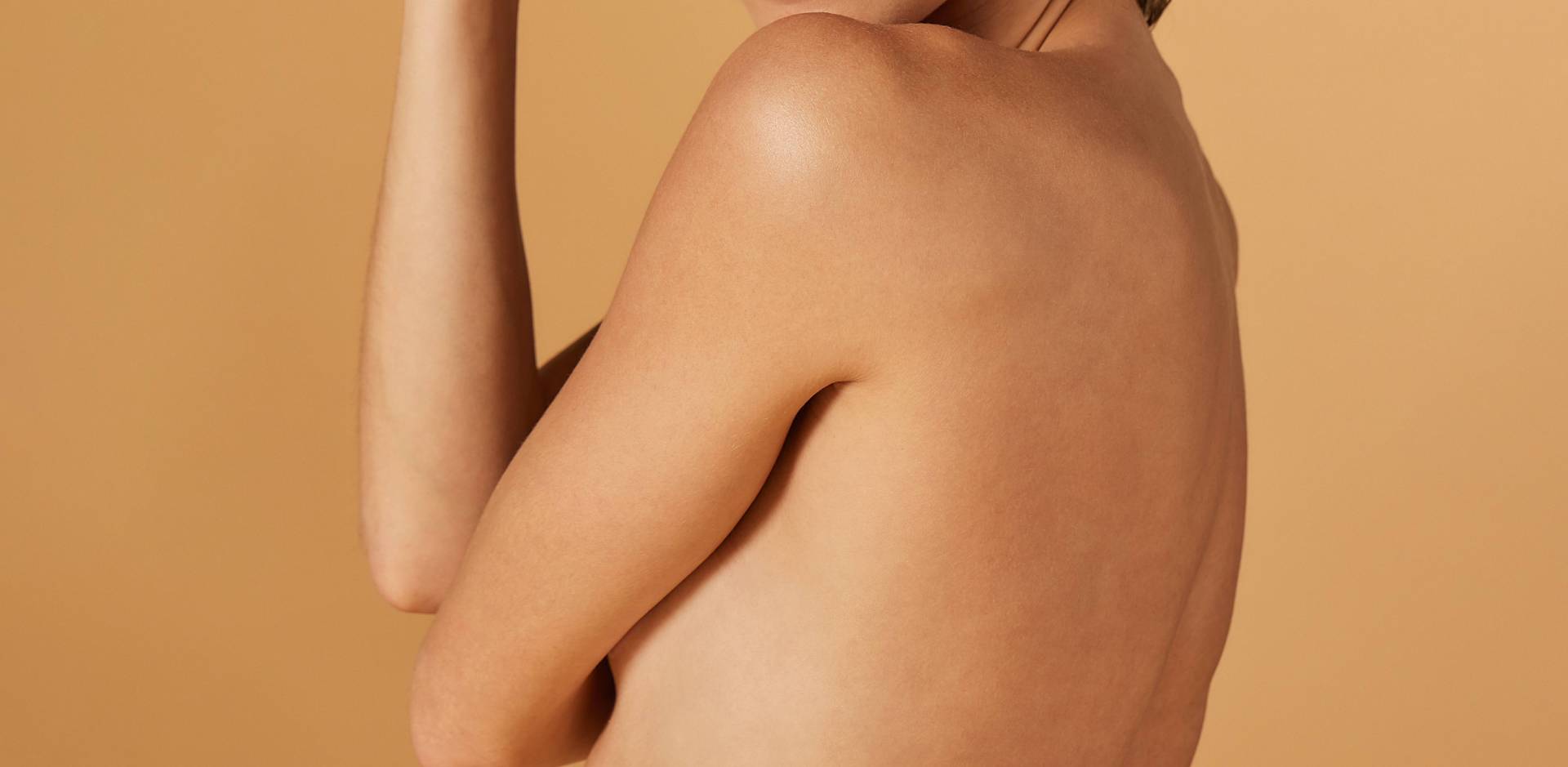 Vue de dos d'une personne à la peau claire et aux cheveux courts, sur un fond beige uni.