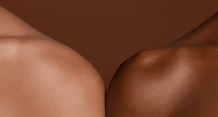 Gros plan sur les épaules de deux personnes, l'une à la peau claire et l'autre à la peau foncée, se touchant délicatement pour symboliser la diversité et la connexion.