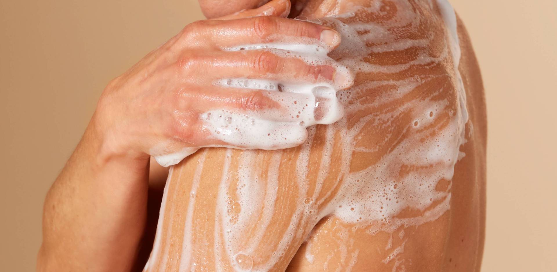 Gros plan sur une personne qui se savonne l'épaule et le bras avec une mousse de douche riche et onctueuse.