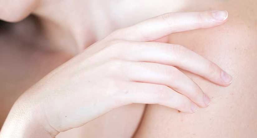 Gros plan sur une main à la peau claire et aux ongles soignés, posée délicatement sur une épaule.
