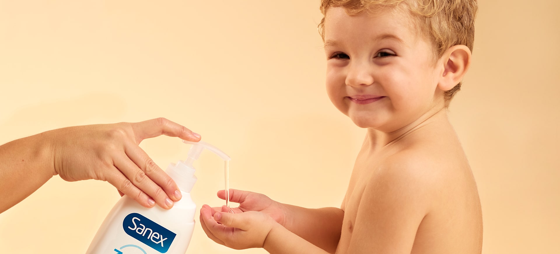 Un jeune enfant souriant tend ses mains pour recevoir du savon liquide Sanex qu'un adulte verse depuis un flacon à pompe.