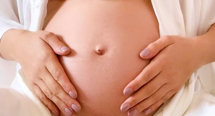 Gros plan sur le ventre nu d'une femme enceinte, ses deux mains aux ongles soignés posées délicatement de chaque côté.