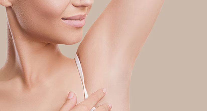 Gros plan sur l'aisselle lisse et nette d'une femme à la peau claire, sa main touchant le bas de son aisselle.