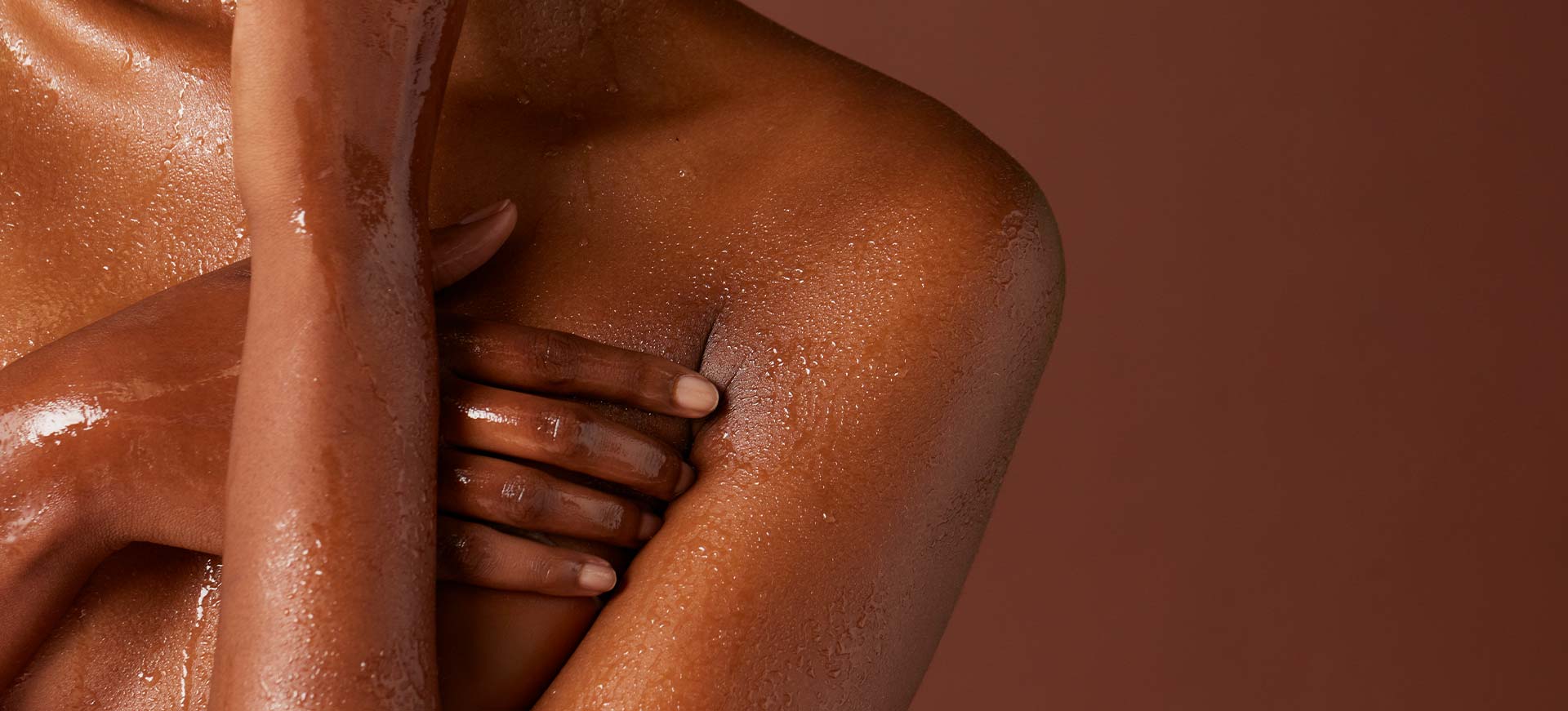  Gros plan sur le buste d'une femme noire à la peau humide et brillante, ses bras croisés sur sa poitrine.