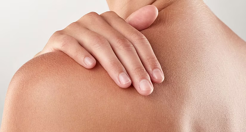 Gros plan sur une main aux ongles soignés posée délicatement sur une épaule à la peau saine.