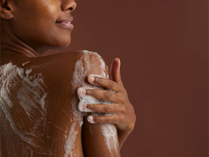Gros plan sur une femme noire vue de dos, se savonnant l'épaule
