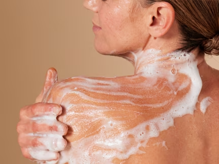 Gros plan sur une femme à la peau mature qui se savonne l'épaule avec une mousse de douche riche et onctueuse.