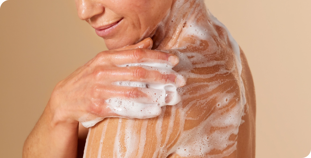 Gros plan sur une femme à la peau mature qui se savonne l'épaule avec une mousse de douche riche et onctueuse.