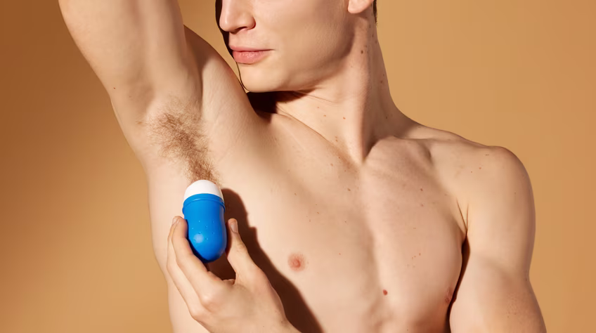 Gros plan sur un homme au torse nu qui lève le bras pour s'appliquer un déodorant roll-on bleu sur son aisselle.